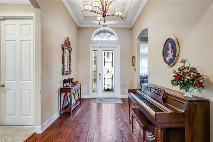 Entryway featuring arched walkways, hardwood / wood-style floors, a chandelier, crown molding, and baseboards