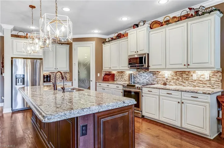 Kitchen with appliances with stainless steel finishes, a sink, a chandelier, a kitchen island with sink, and hardwood / wood-style flooring