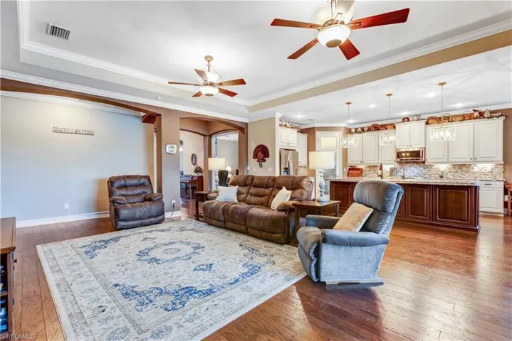 Living room with arched walkways, ceiling fan, hardwood / wood-style flooring, ornamental molding, and baseboards