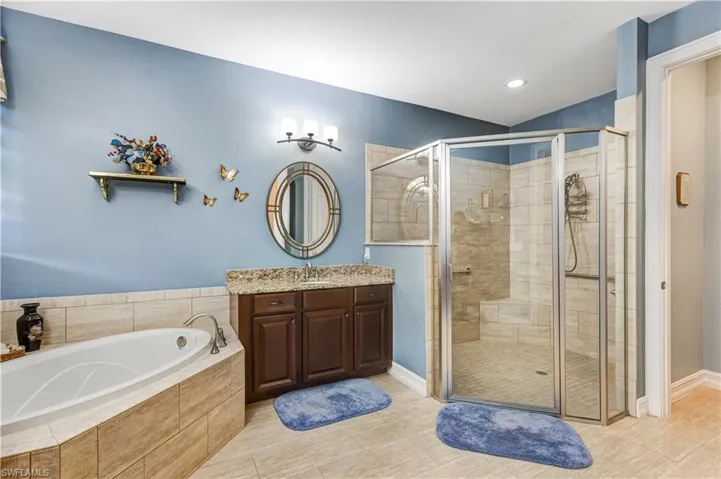Bathroom featuring a stall shower, a garden tub, vanity, baseboards, and recessed lighting
