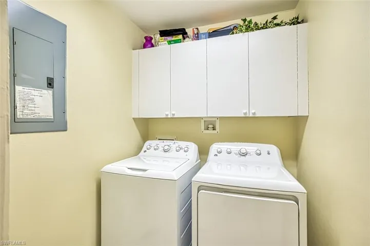 Clothes washing area featuring washing machine and dryer, cabinet space, and electric panel
