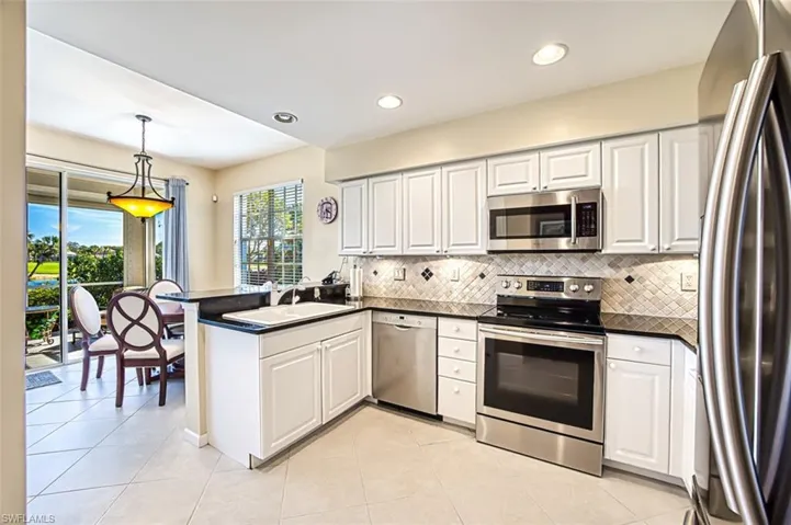 Kitchen with decorative light fixtures, dark countertops, appliances with stainless steel finishes, white cabinetry, and a peninsula