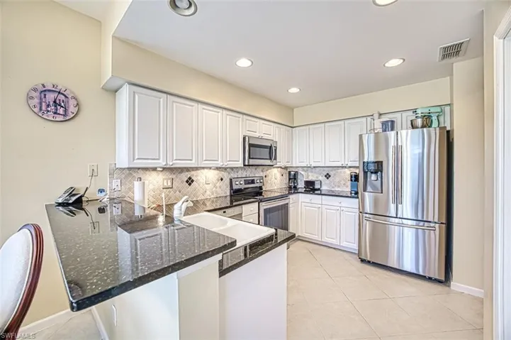 Kitchen featuring visible vents, appliances with stainless steel finishes, white cabinets, dark stone counters, and a peninsula