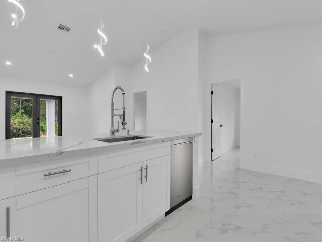 Kitchen with light stone countertops, visible vents, white cabinetry, a sink, and dishwasher