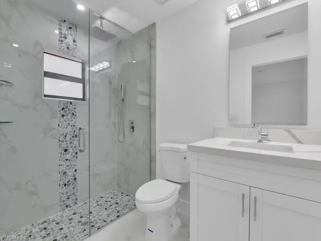 Bathroom with a marble finish shower, visible vents, toilet, marble finish floor, and vanity