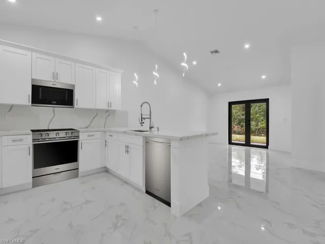 Kitchen with lofted ceiling, recessed lighting, appliances with stainless steel finishes, marble finish floor, and a sink