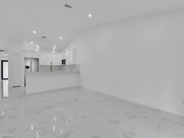 Unfurnished living room featuring lofted ceiling, baseboards, marble finish floor, and a sink