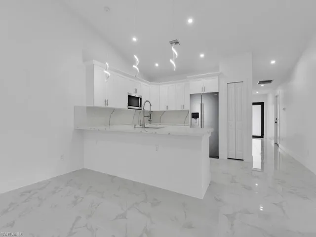 Kitchen featuring white cabinetry, light countertops, a peninsula, marble finish floor, and stainless steel appliances