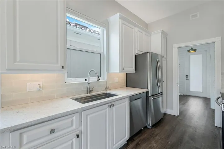 Kitchen with stainless steel appliances, a sink, white cabinetry, and tasteful backsplash
