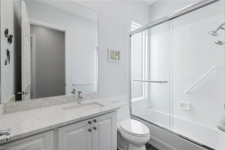 Guest Bathroom with vanity, toilet, and enclosed tub / shower combo. Note: Dated standard glass bricks were replaced with beautiful Impact Glass.