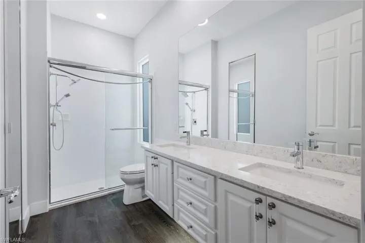 Master Bathroom with double vanity, a shower stall, toilet, and recessed lighting. Note: Dated glass bricks in shower have been replaced with beautiful Impact Glass.