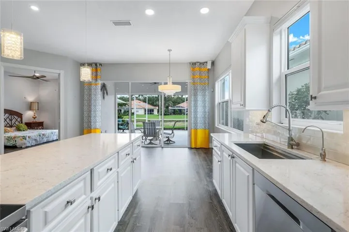 Kitchen featuring dishwasher, a sink, dark wood-style luxury vinyl floors, white cabinetry, and recessed lighting