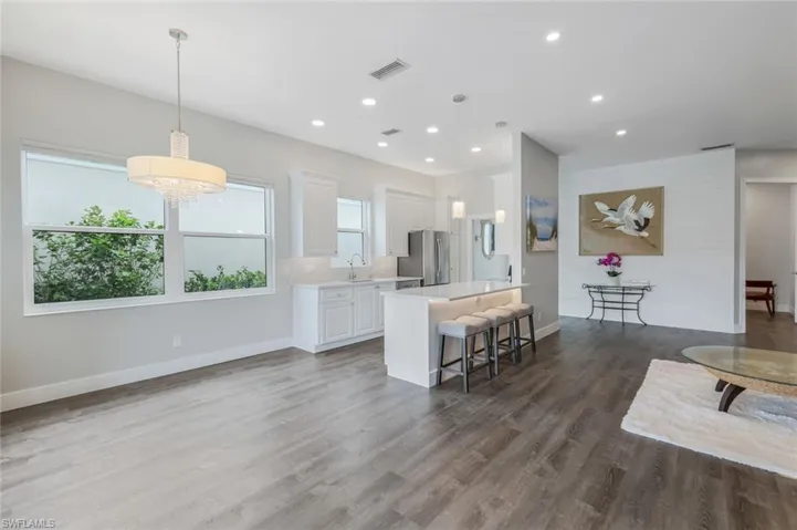 Kitchen with freestanding refrigerator, light countertops, a kitchen bar, white cabinetry, and wood finished floors