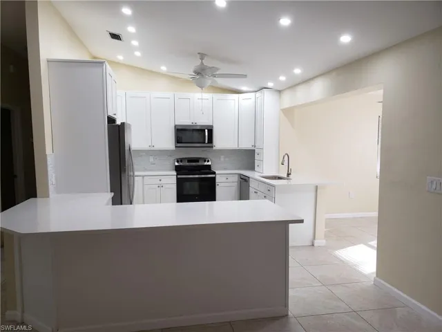 Kitchen with a peninsula, stainless steel appliances, white cabinets, backsplash, and recessed lighting