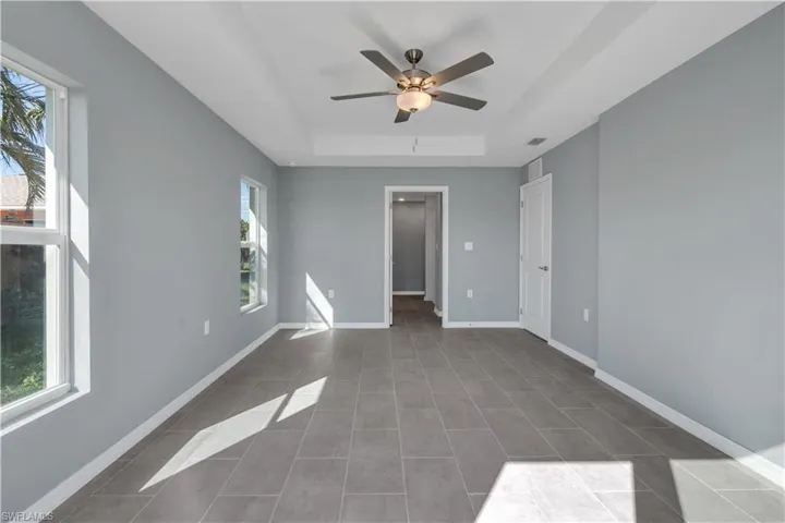 Spare room featuring a raised ceiling, visible vents, a ceiling fan, dark tile patterned floors, and baseboards