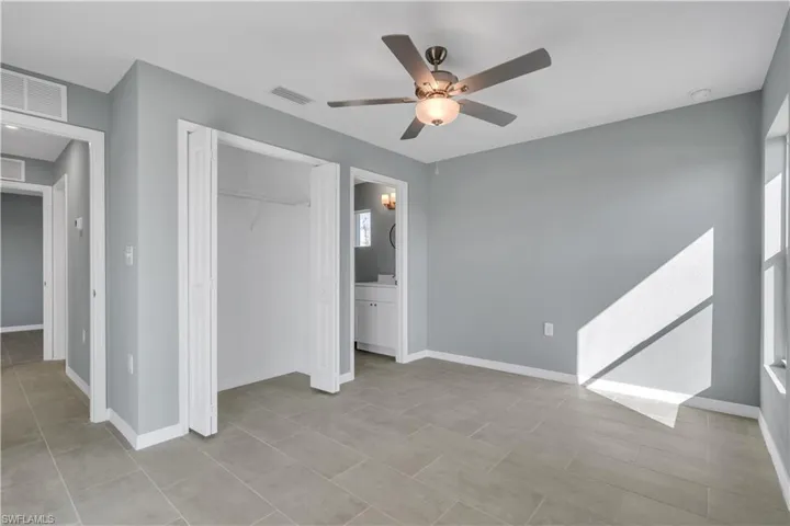 Unfurnished bedroom with a closet, visible vents, a ceiling fan, ensuite bath, and baseboards