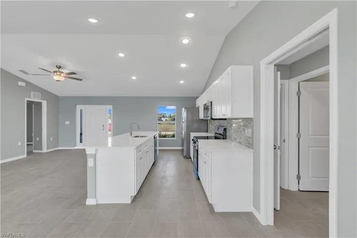 Kitchen featuring white cabinets, lofted ceiling, appliances with stainless steel finishes, light countertops, and a sink