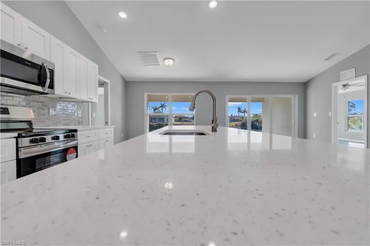 Kitchen with visible vents, decorative backsplash, light stone countertops, stainless steel appliances, and a sink