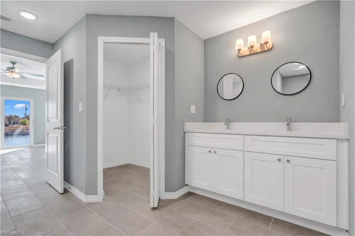 Full bathroom with double vanity, baseboards, a ceiling fan, a spacious closet, and a sink