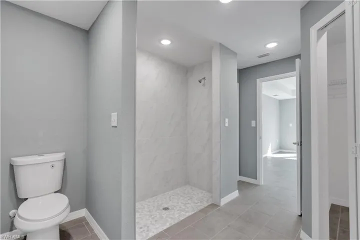 Bathroom with visible vents, toilet, walk in shower, baseboards, and tile patterned floors