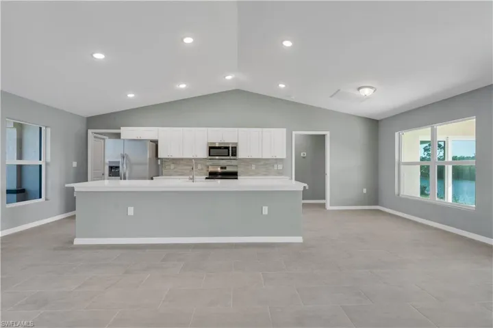 Kitchen featuring stainless steel appliances, a spacious island, white cabinets, light countertops, and backsplash