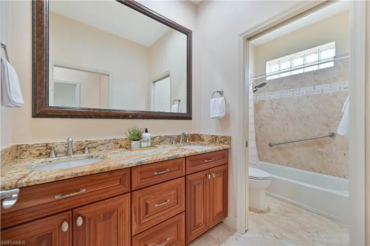 Bathroom featuring a dual vanity with a granite countertop, wood-finish cabinetry, and an ornate framed mirror