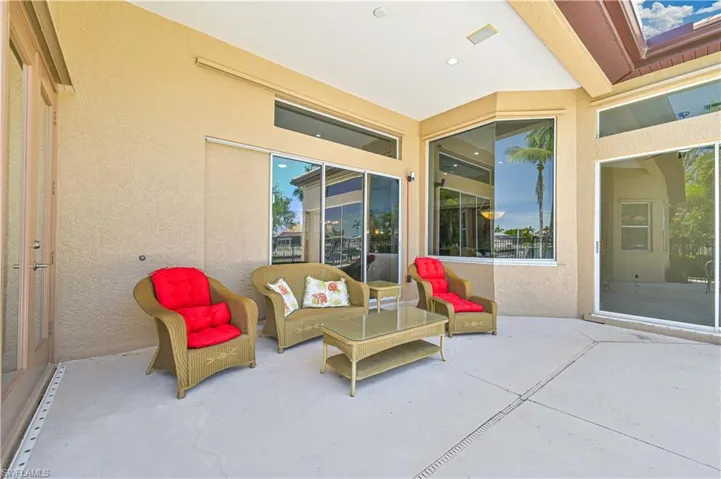 Spacious covered patio featuring textured stucco walls, multiple large windows, a glass-paneled door, and recessed lighting