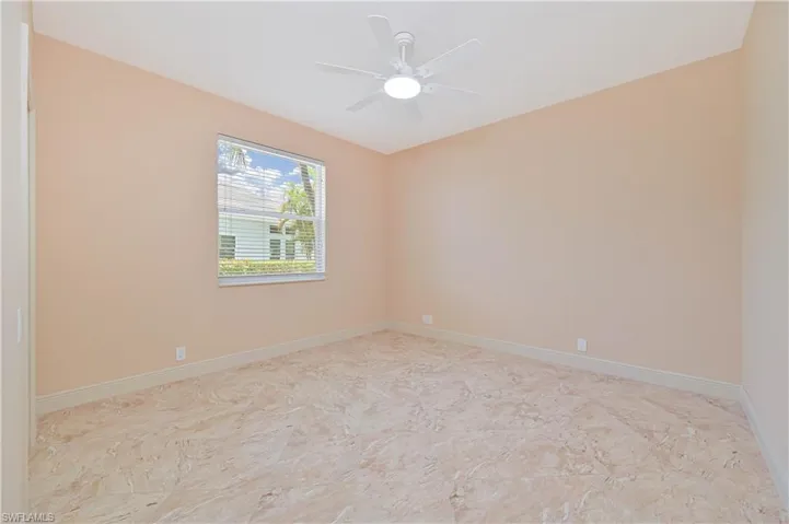 Spacious room featuring neutral wall tones, large window with blinds, ceiling fan, and light-toned tile flooring