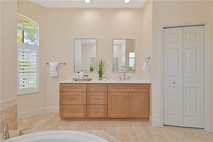 Double vanity featuring light wood-finish cabinetry, a light-toned countertop, and dual mirrors