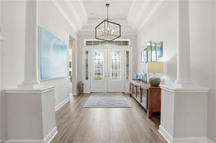 Grand entryway featuring double glass-panel doors, wood-finish flooring, a coffered ceiling, and decorative columns