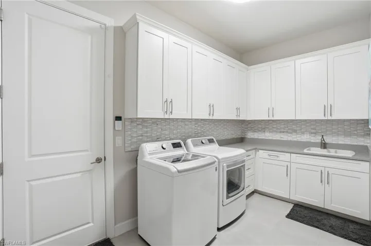 Dedicated laundry area featuring abundant white shaker-style cabinetry, a built-in sink with a gooseneck faucet, gray countertops, a mosaic tile backsplash, and light gray flooring