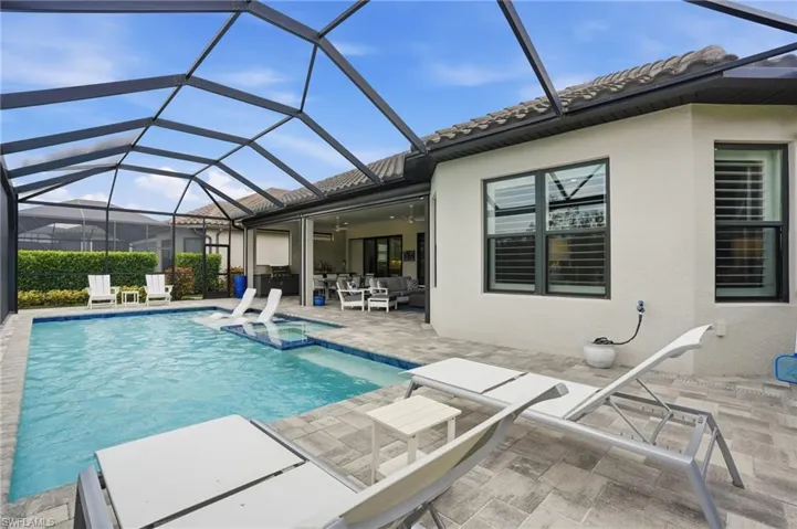 Screened outdoor living area featuring a swimming pool with integrated spa and sun shelf