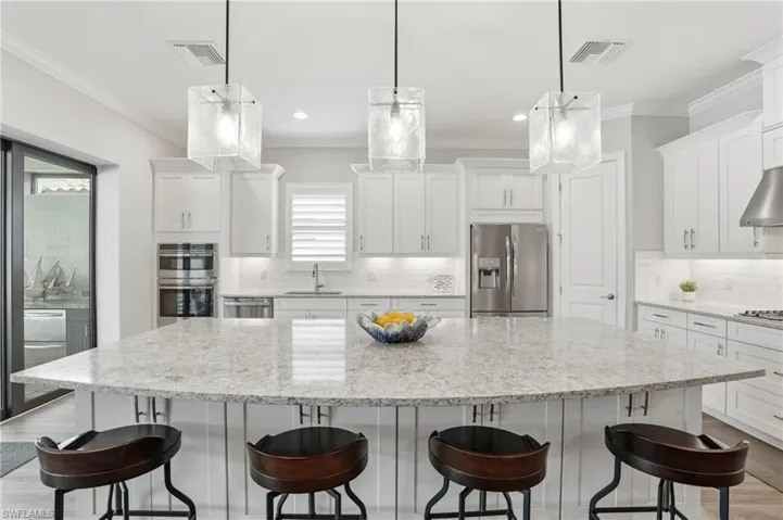 Kitchen featuring a large central island with a light-colored countertop, white cabinetry with crown molding, stainless steel appliances, and pendant lighting fixtures