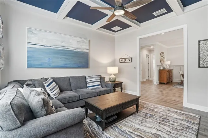 Coffered ceiling with a painted blue inset, wood-finish flooring, and an open-frame doorway leading to an additional space