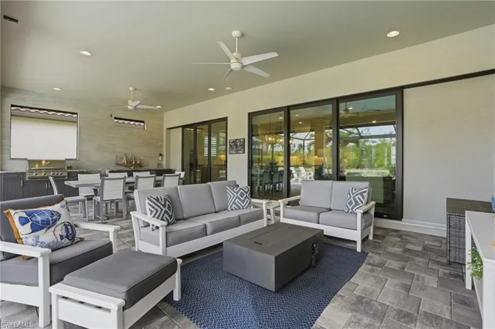 Expansive covered patio featuring paver flooring, multiple ceiling fans, recessed lighting, an integrated outdoor kitchen with built-in grill, and large sliding glass doors providing access to interior spaces