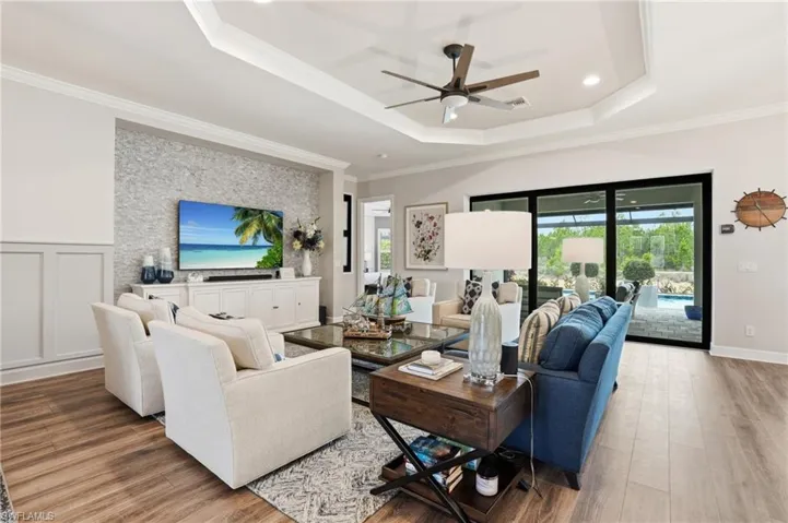 Spacious living area featuring wood-finish flooring, a tray ceiling with a fan, and a built-in entertainment center with a textured accent wall