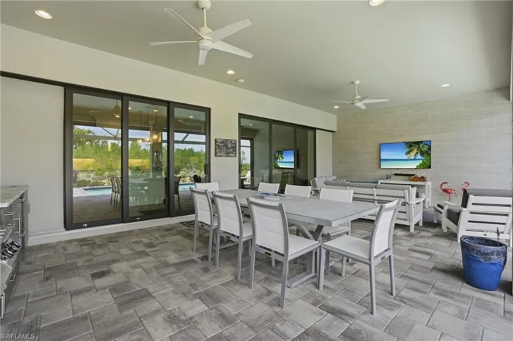 Covered outdoor living space featuring paver flooring, multiple ceiling fans, recessed lighting, and expansive sliding glass doors