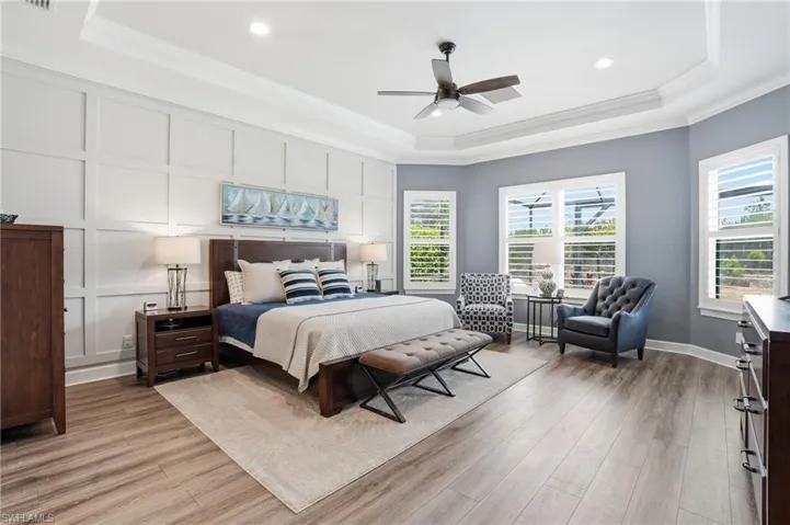 Wood-finish flooring throughout, tray ceiling with a ceiling fan, recessed lighting, and white plantation shutters on multiple windows