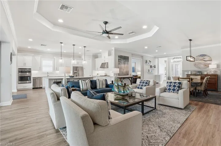 Open-concept living area featuring wood-finish flooring, a tray ceiling with recessed lighting and a ceiling fan, and a kitchen with white cabinetry and stainless steel appliances
