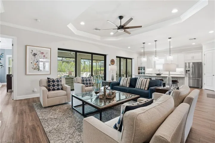 Open concept living space featuring wood-finish flooring, a tray ceiling with a ceiling fan, crown molding, and recessed lighting