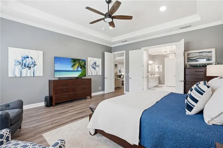 Tray ceiling with crown molding, wood-finish flooring, and a ceiling fan