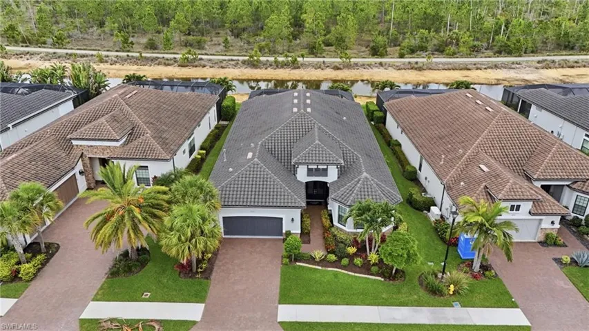 Exterior showcasing a tile roof, paver driveway, manicured landscaping, and a canal at the rear of the property