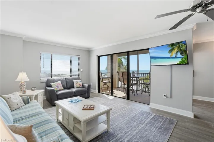 Living room with ceiling fan, wood finished floors, crown molding, and plenty of natural light
