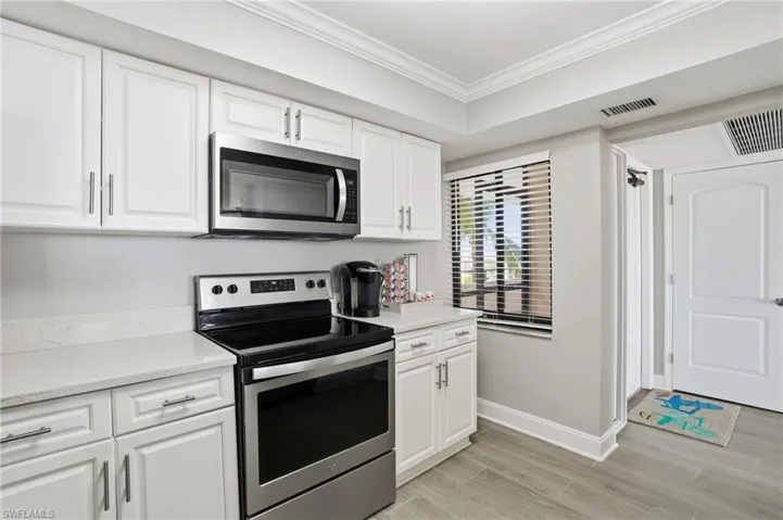 Kitchen featuring stainless steel appliances, white cabinets, crown molding, light wood-style flooring, and light stone counters