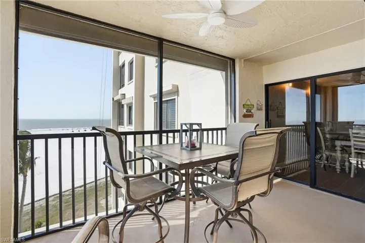 Sunroom with view of water and beach, outdoor dining space, a ceiling fan, and healthy amount of natural light