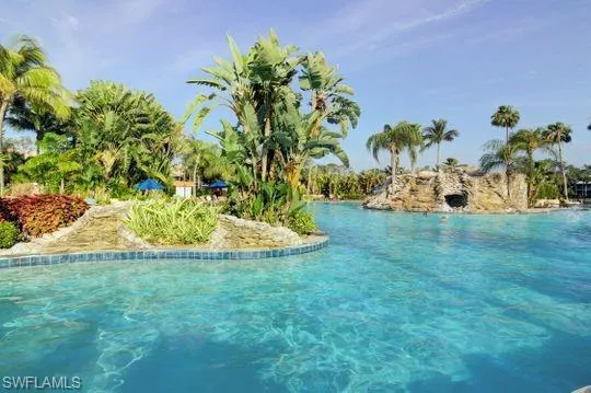 Expansive swimming pool with integrated rock formation, lush tropical landscaping, and a blue-tiled perimeter