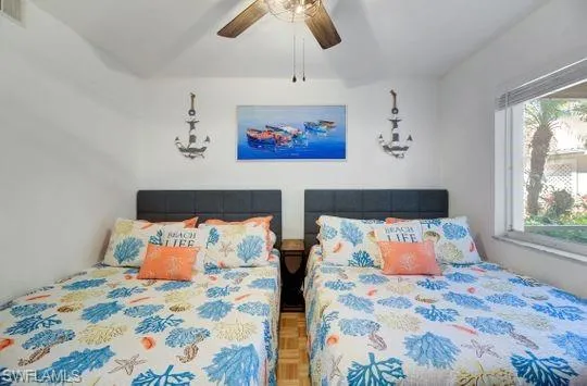 White walls with a ceiling fan, two beds with fabric headboards, and a window with blinds