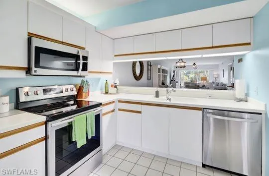 White cabinetry with wood-finish trim, stainless steel appliances, white countertops, and a mirrored backsplash