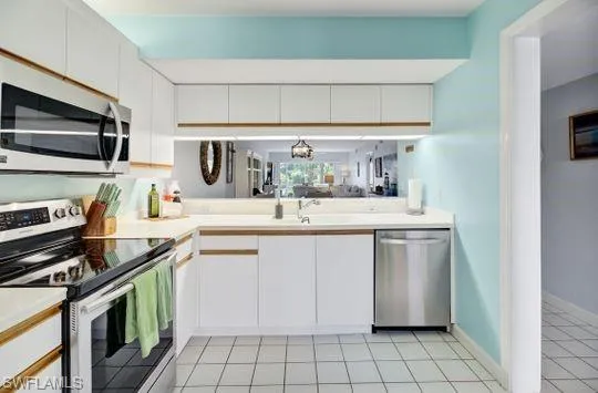 White cabinetry with wood-finish accents, stainless steel appliances, solid surface countertops, and white square tile flooring