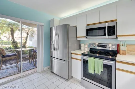Kitchen featuring stainless steel appliances, white cabinetry with wood trim, white countertops, and white tile flooring